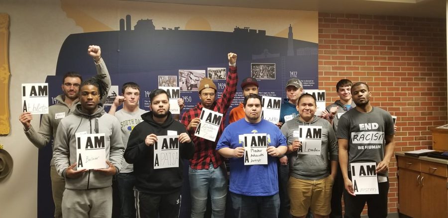 Men who attended the moment of brotherhood pose with signs that describe who they are, like a leader or artist. 