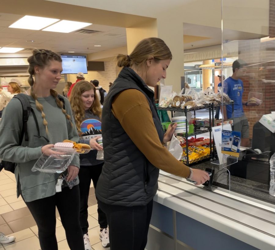 Collegian photo by KAITLYN LORANG 
Leah Irlbeck taps her phone to pay for her meal recently at The Market in the University Student Union. Friends Keelie Van Hee and Andrea Eisenschenk wait for their turn.