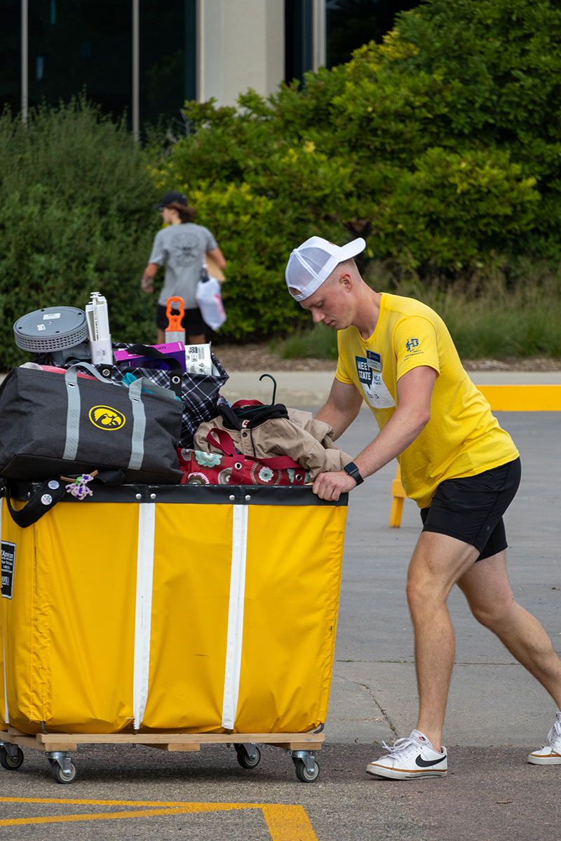 A CA pushes around an overflowing  cart filled with luggage during new student move-in.