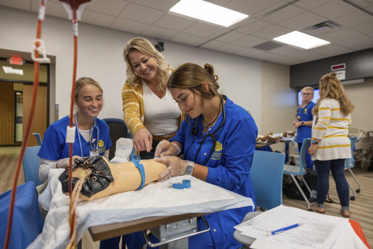 Nursing students insert an IV into a prosthetic arm. 