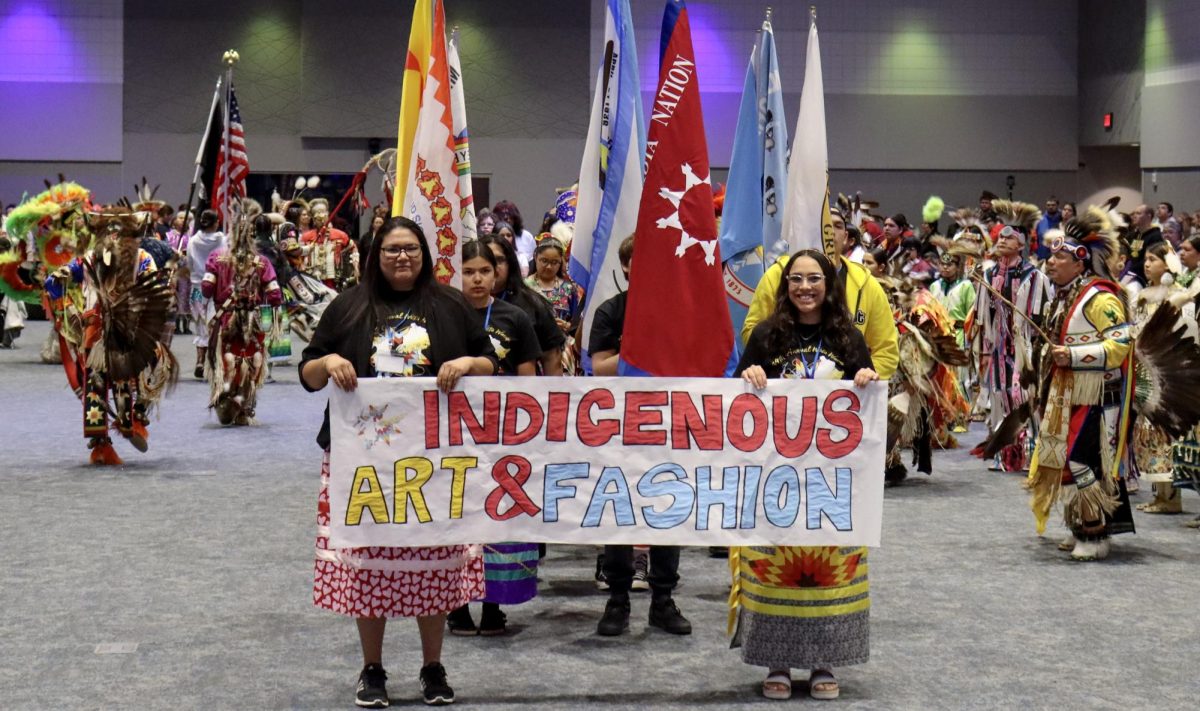 Marisa Hare (Left) and Alejandra Juarez (Right) hold up the Indigenous Art and Fashion sign during the first Grand Entry at the 34th Annual AISA Wetu Wacipi, Saturday, March 28, 2026. The American Indian Student Association held their 34th Annual Wetu Wacipi March 28 and 29, 2026.